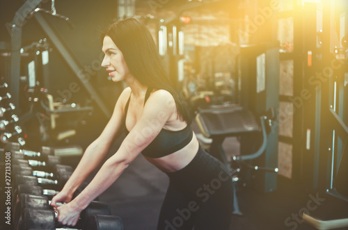 Young fit woman taking a dumbbell from the rack in the gym.