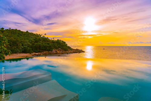 Beautiful outdoor infinity swimming pool with coconut palm tree around beach sea ocean at sunrise or sunset time