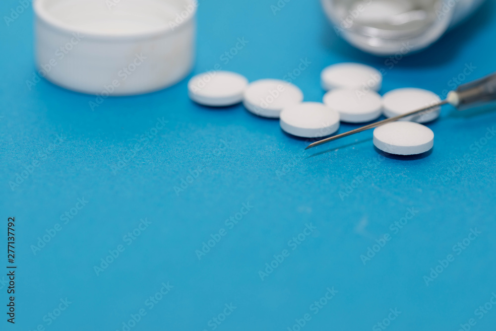 White pills and syringe close up macro shot on blue background, copy space. White pills and syringe close up macro shot on blue background, copy space.