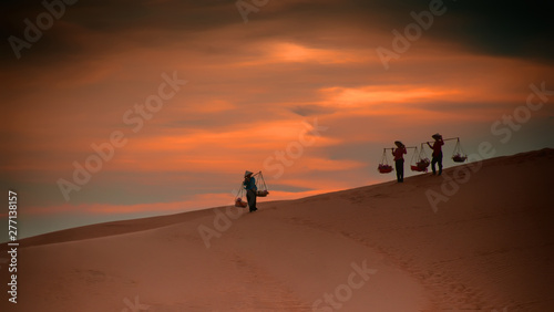 Lifestyle of Asian women carrying baskets on her shoulders in the desert at sunset or sunrise time, Mui Ne, Vietnam.Asian women is walking and carry basket. 