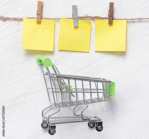 Blank paper stickers with copy space and a shopping cart on a white table background. Shopping list template.