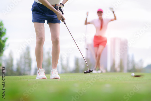 young woman golf player failed to putting golf ball into the hole on the green of the golf course, cheerfully and happiness on the failure of the opponent competitor in background