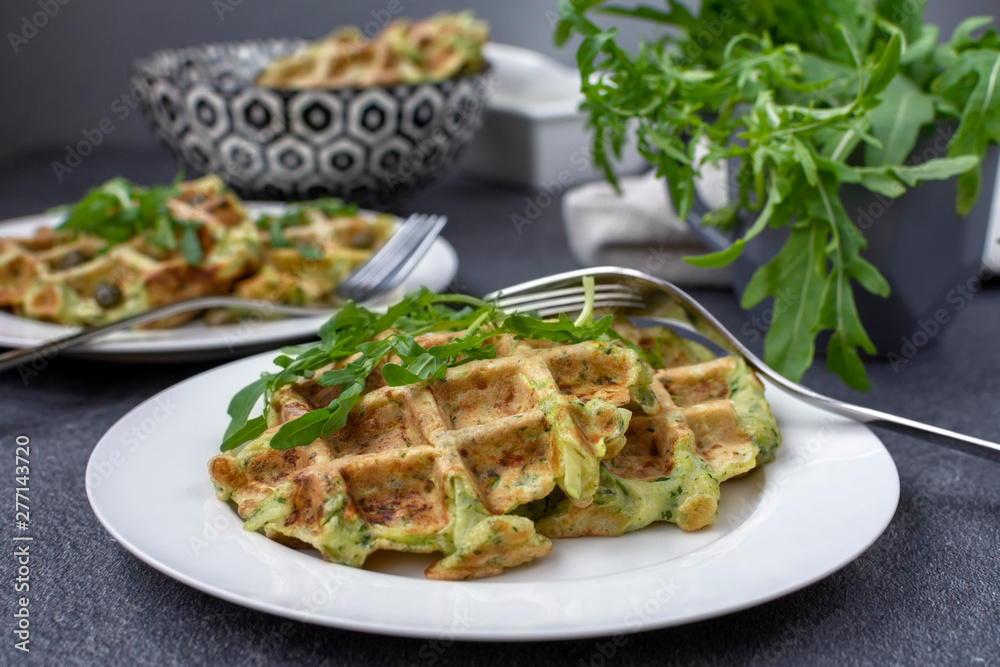 Homemade fresh baked zucchini waffles, served with fresh arugula on white plate Homemade fresh baked zucchini waffles, served with fresh arugula on white plate