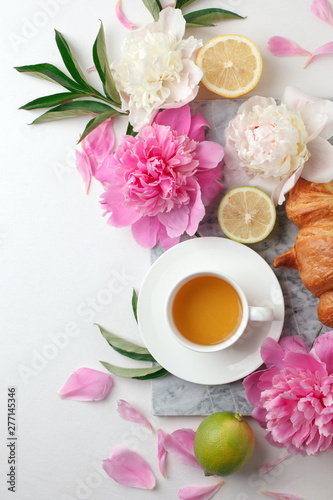 Morning cup of tea and fresh beautiful pink and white peony flowers on white background. Top view. Flat layout, concept of female holiday morning, stylish blogger