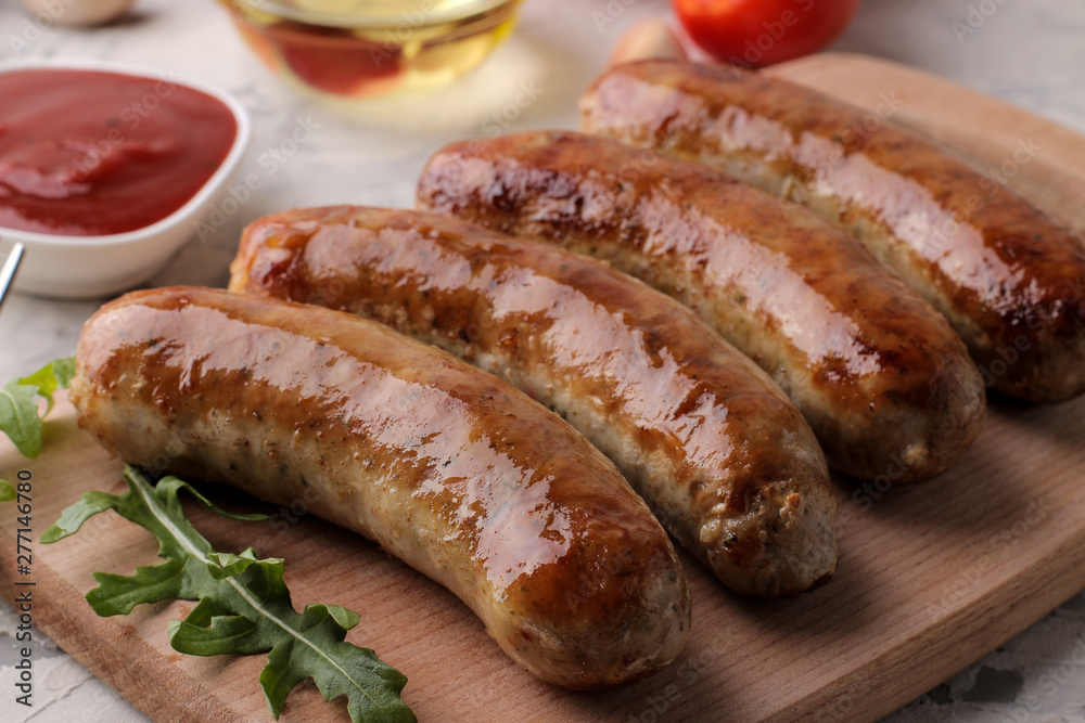 Delicious grilled sausages on a board with red sauce and spices on a light background. B-B-Q. Delicious grilled sausages on a board with red sauce and spices on a light background. B-B-Q.