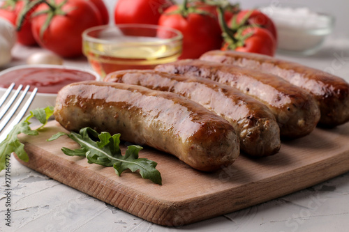 Delicious grilled sausages on a board with red sauce and spices on a light background. B-B-Q.