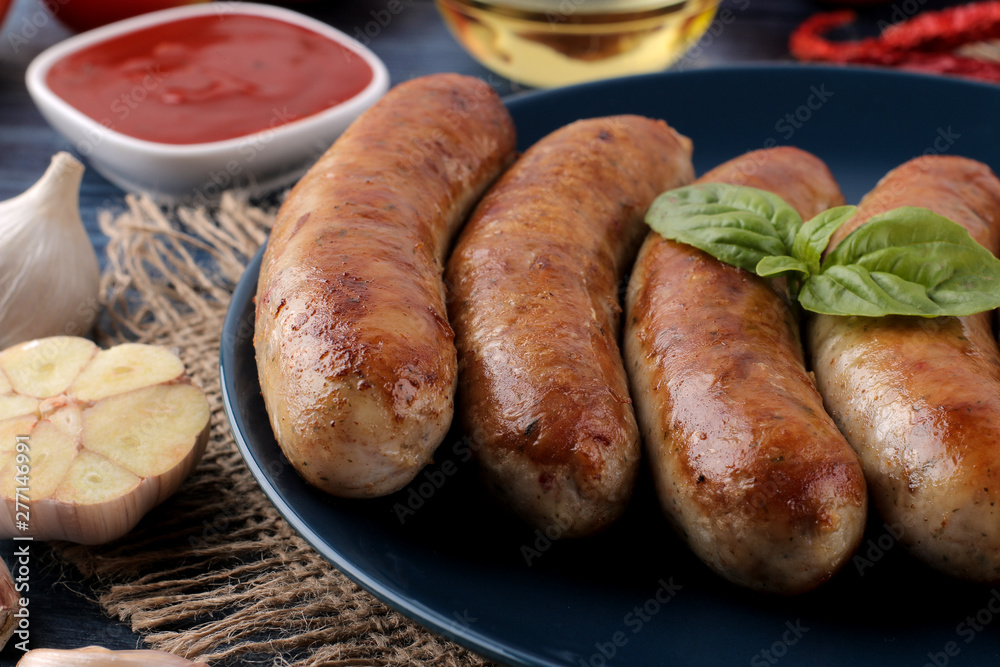 Delicious grilled sausages on a plate with red sauce and spices on a blue wooden background. B-B-Q. Delicious grilled sausages on a plate with red sauce and spices on a blue wooden background. B-B-Q.