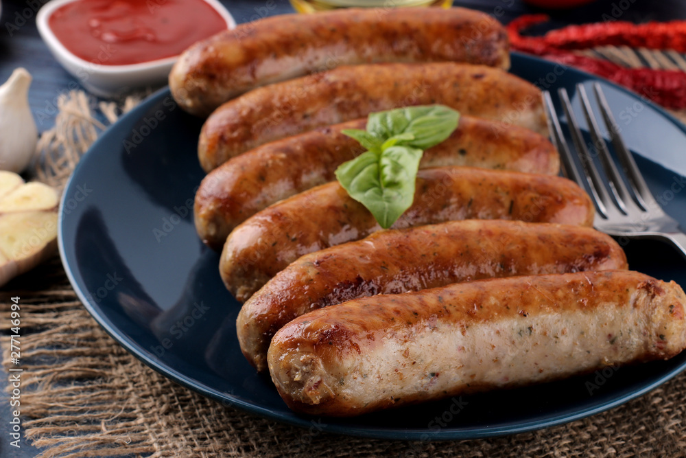 Delicious grilled sausages on a plate with red sauce and spices on a blue wooden background. B-B-Q. Delicious grilled sausages on a plate with red sauce and spices on a blue wooden background. B-B-Q.
