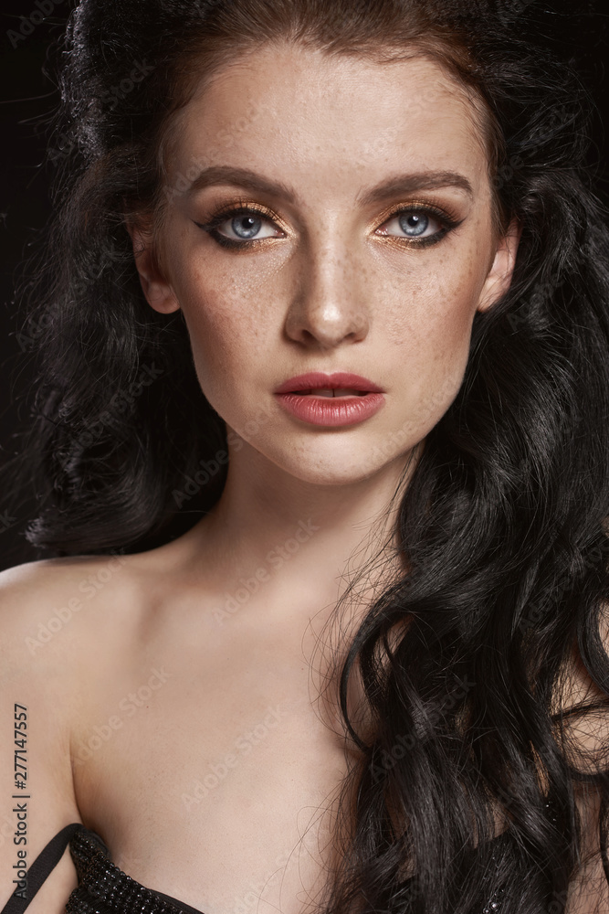 Fototapeta premium Beautiful brunette girl with clean skin and make-up in black dress on black background. Dramatic portrait. Closeup portrait.
