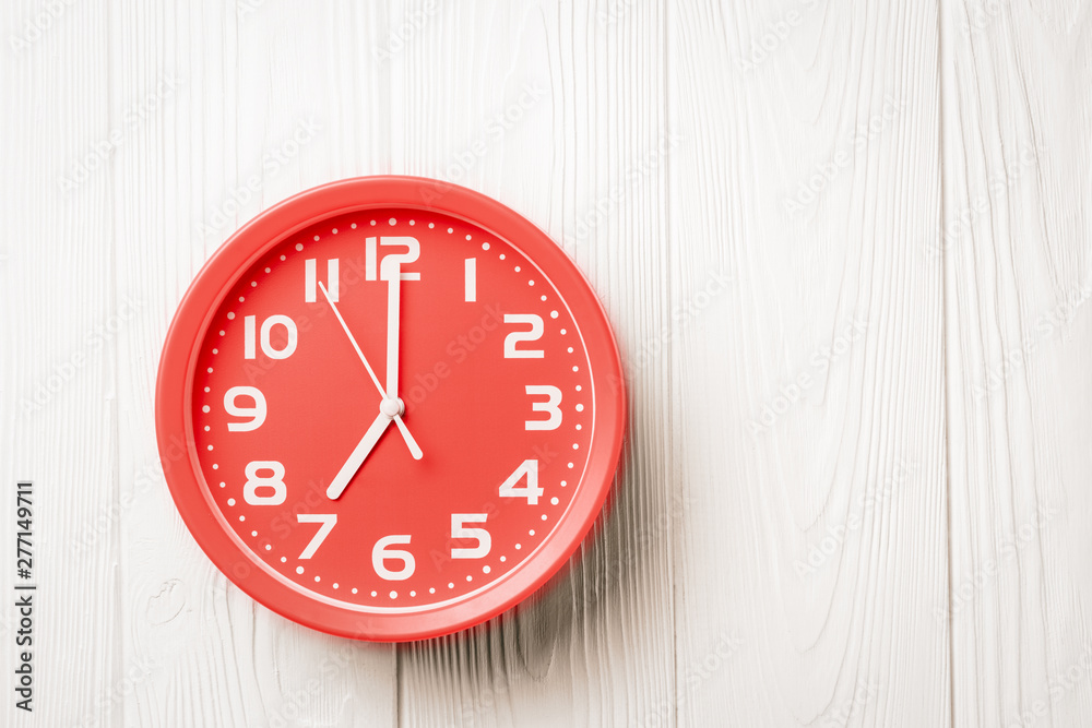 Top view red clock showing seven o'clock on a white wooden background Top view red clock showing seven o'clock on a white wooden background