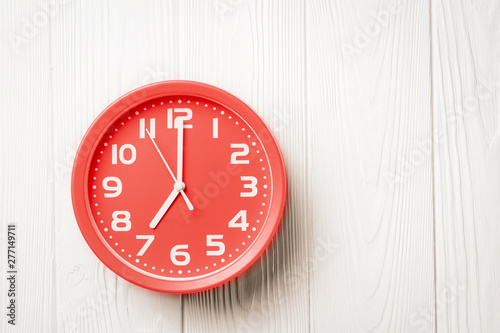 Top view red clock showing seven o'clock on a white wooden background