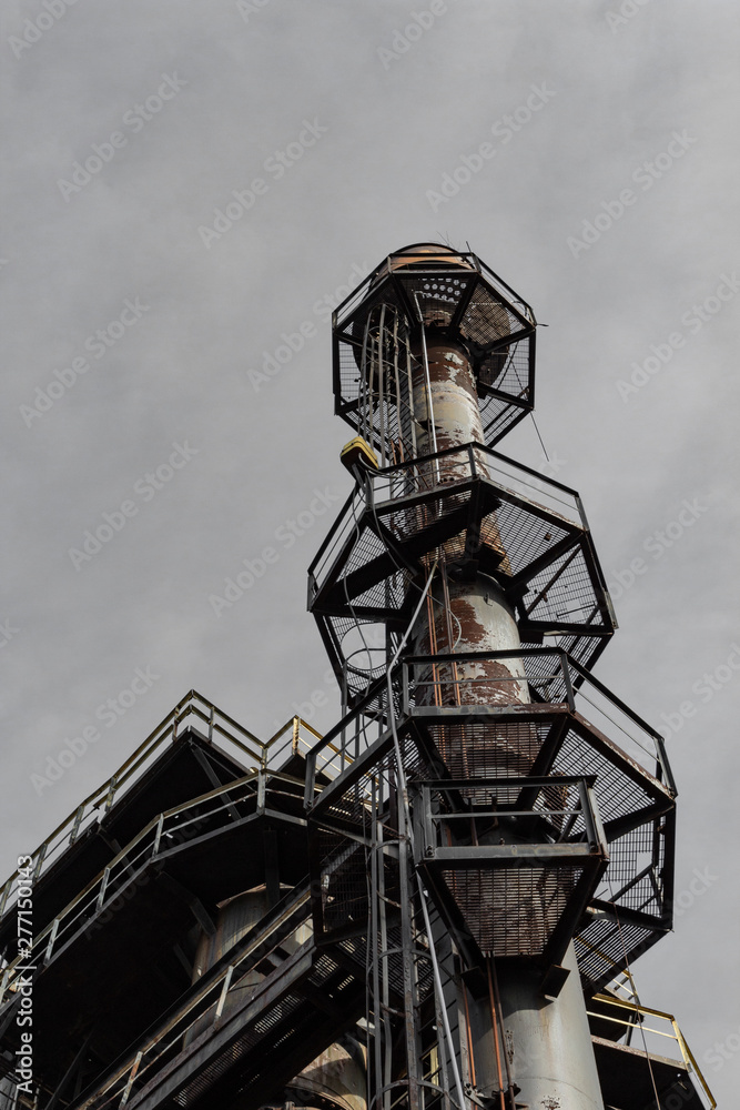 Ladders and expanded metal walkways around a smokestack, urban industrial steel mill, vertical aspect Ladders and expanded metal walkways around a smokestack, urban industrial steel mill, vertical aspect