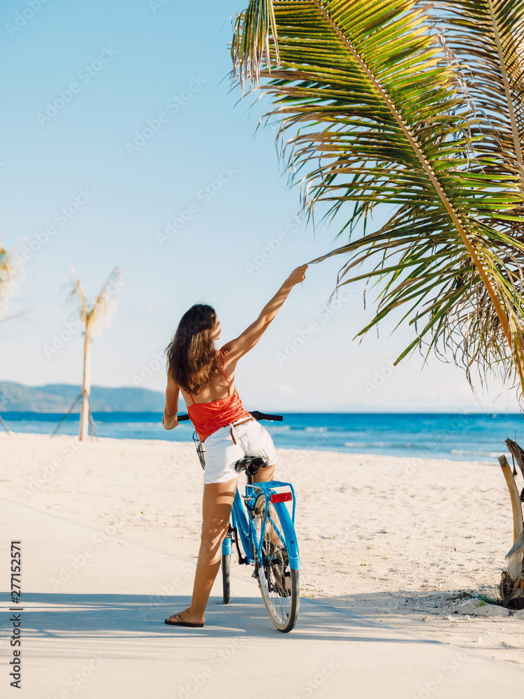 Happy young woman on blue bicycle near ocean in tropical island Happy young woman on blue bicycle near ocean in tropical island