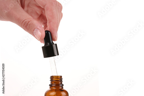 Cosmetic pipette in the hand on white background. Essential oil falling from glass dropper