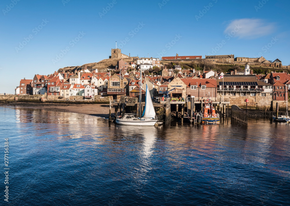 Whitby harbour on a clear day showing the quayside and the church on the hill with a boat moored by the side of Whitby’s life boat. 