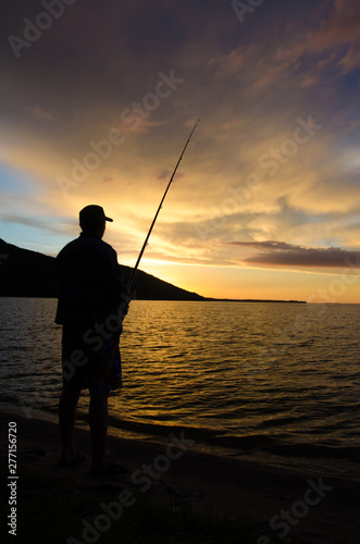 Fisherman fishes lake and mountains at sunset golden summer vacation