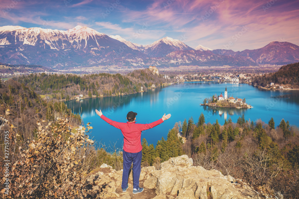 Man with hands in the air standing on a cliff over Bled Lake in early spring. Slovenia, Europe