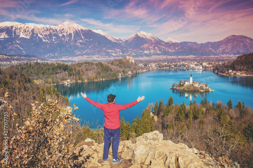 Man with hands in the air standing on a cliff over Bled Lake in early spring. Slovenia, Europe © vvvita