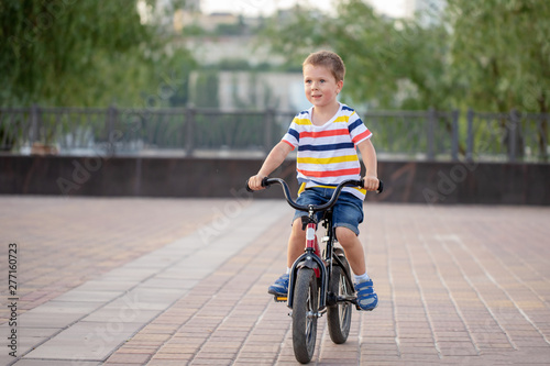 Fototapeta Naklejka Na Ścianę i Meble -  child on a bicycle at asphalt road in early morning. Boy on bike in the city