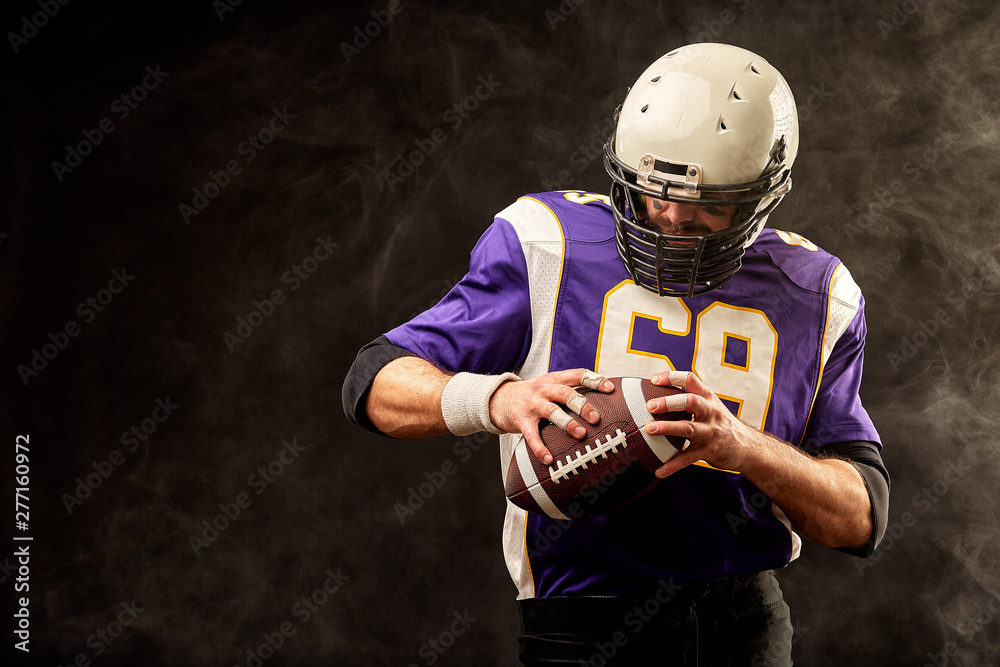 American football player holding ball in his hands in smoke. Black background, copy space. The concept of American football, motivation, copy space, Sports banner.