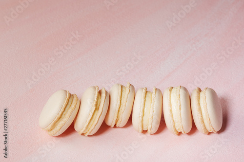 White vanilla macaroons in a row on a light pink background.