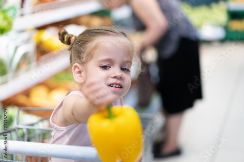 Little Caucasian girl chooses fresh vegetables in the supermarket.