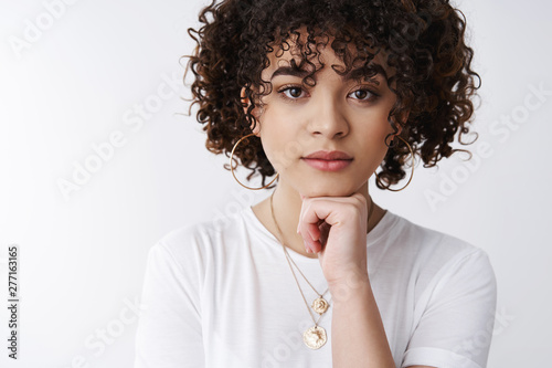 Thoughtful powerful good-looking curly-haired stylish 25s woman hold hand face-line gaze camera confident alluring listen intersting story thinking, taking important decision, white background photo