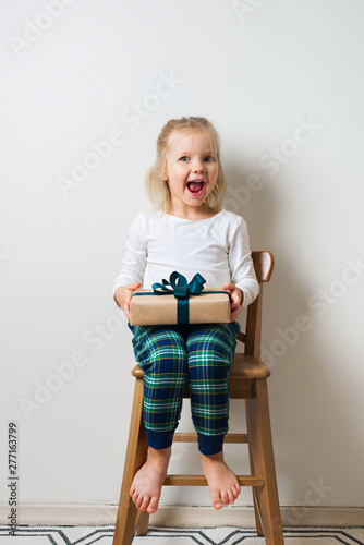 Scandinavian minimalism christmas and new year concept with kid - little girl with stack of gift box on a chair in room