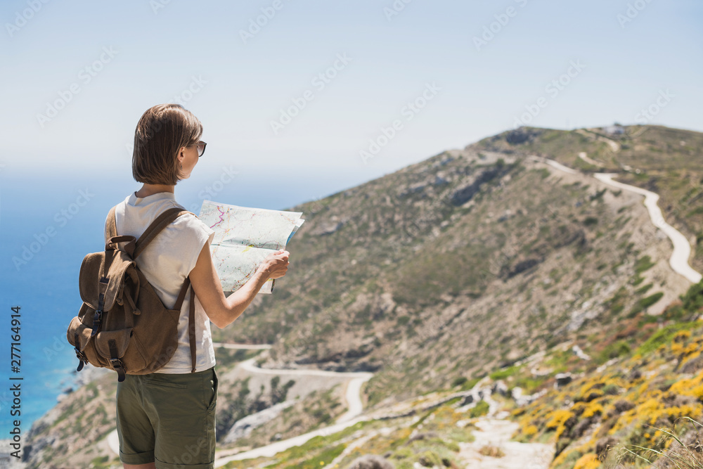 Woman traveler with backpack holding map. Travel, tourism, summer holidays, active lifestyle concept. Hipster tourist girl looking for hiking route with sea and mountain at background