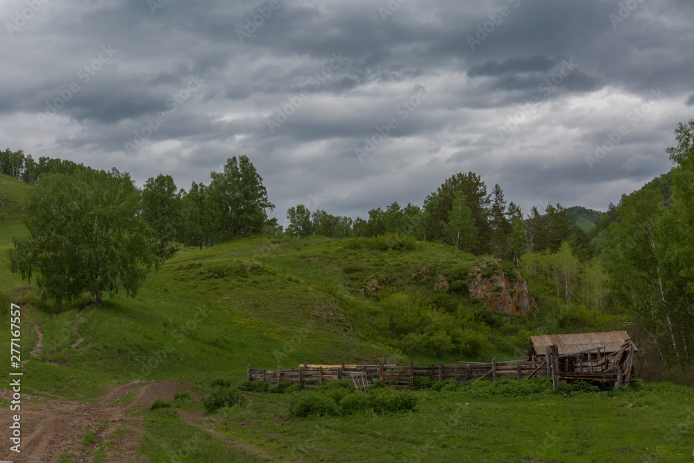 Old abandoned barn in the mountains. The road leading to the barn against the backdrop of mountains and cloudy sky Old abandoned barn in the mountains. The road leading to the barn against the backdrop of mountains and cloudy sky