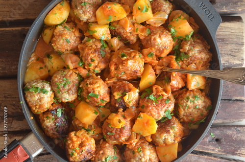 Fried meatballs with potatoes in a pan on a wooden background