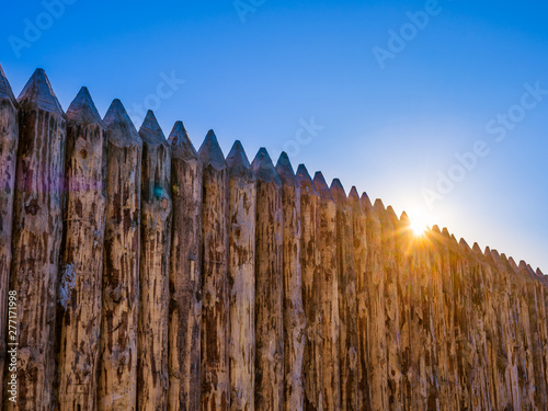 Wooden wall of the fort from vertical logs close-up. The setting sun can be seen on the edge of the wall.