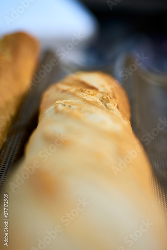 Detailed macro close up shot of french bread baguette out of oven fresh warm cooked baked crunchy crust toast disposed in metallic oven professional special trays.