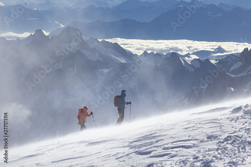 Equipped climber ascent by snowy slope with climbing rope on the top of peak in snowy alpine mountains. Life guard professional man on the work in high mountains. Action in hard conditions scene.