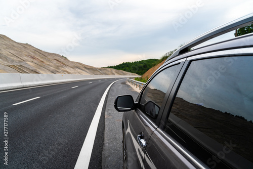 Car parked on highway side with curved road and mountain background