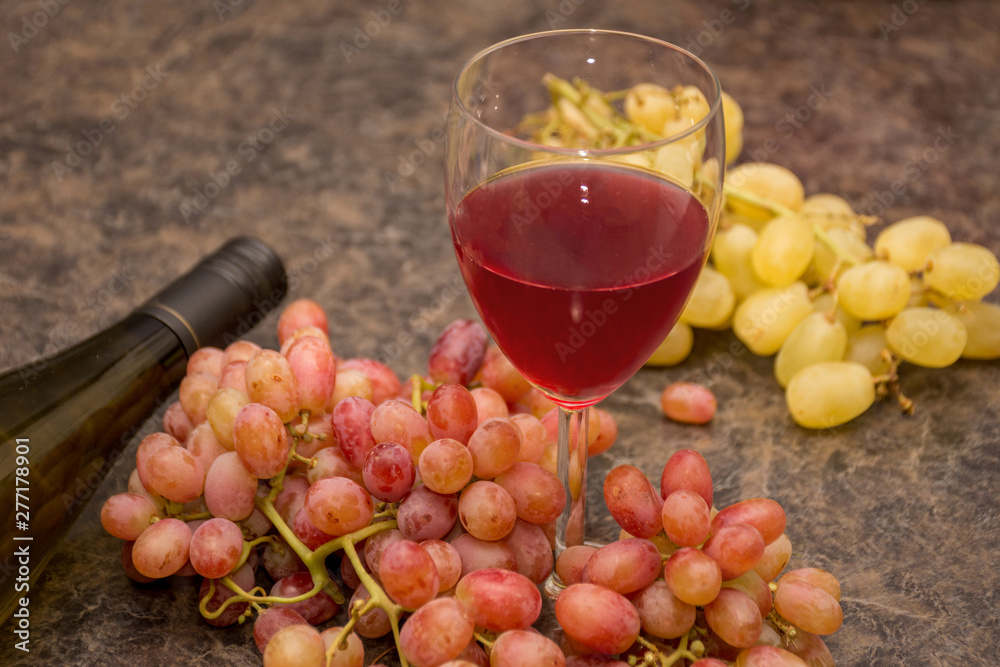 Red and white ripe grapes, wine glass and a bottle of wine on a dark marble background