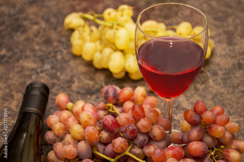 Red and white ripe grapes  wine glass and a bottle of wine on a dark marble background