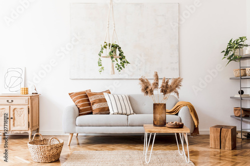 The stylish boho composition at living room interior with design gray sofa, wooden coffee table, commode and elegant personal accessories. Honey yellow pillows and plaid. Cozy apartment. Home decor