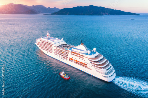 Cruise ship at harbor. Aerial view of beautiful large white ship at sunset. Colorful landscape with boats in marina bay, blue sea, sky. Top view from drone of yacht. Luxury cruise. Floating liner