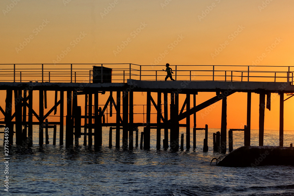 Silhouette of a man who runs along the pier during sunset.