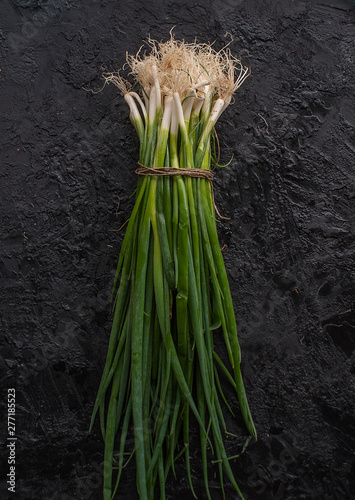 A large bunch of green onions on a black slate background. The concept of a rich harvest. The view from the top. Copy space.