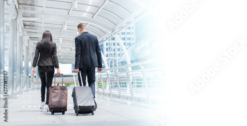 Caucasian businessman and businesswoman walk together with luggage on the public street with copy space, business travel and trip concept