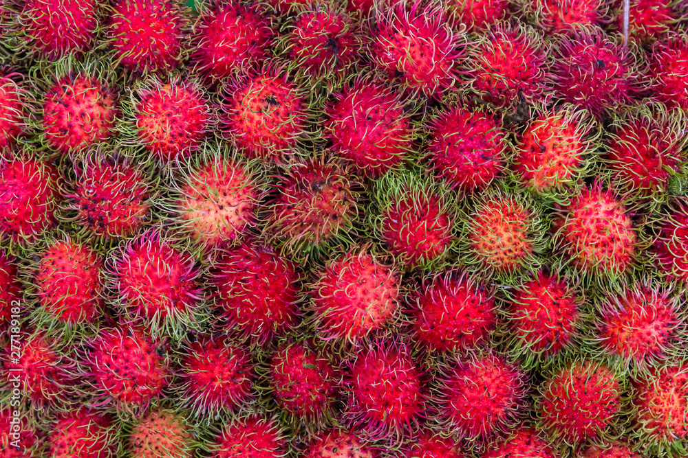 Pile of tropical rambutan fruits. Pink and spiky rambutan are piled on a table at a farmers market. Healthy fruits rambutans background. Pile of tropical rambutan fruits. Pink and spiky rambutan are piled on a table at a farmers market. Healthy fruits rambutans background.