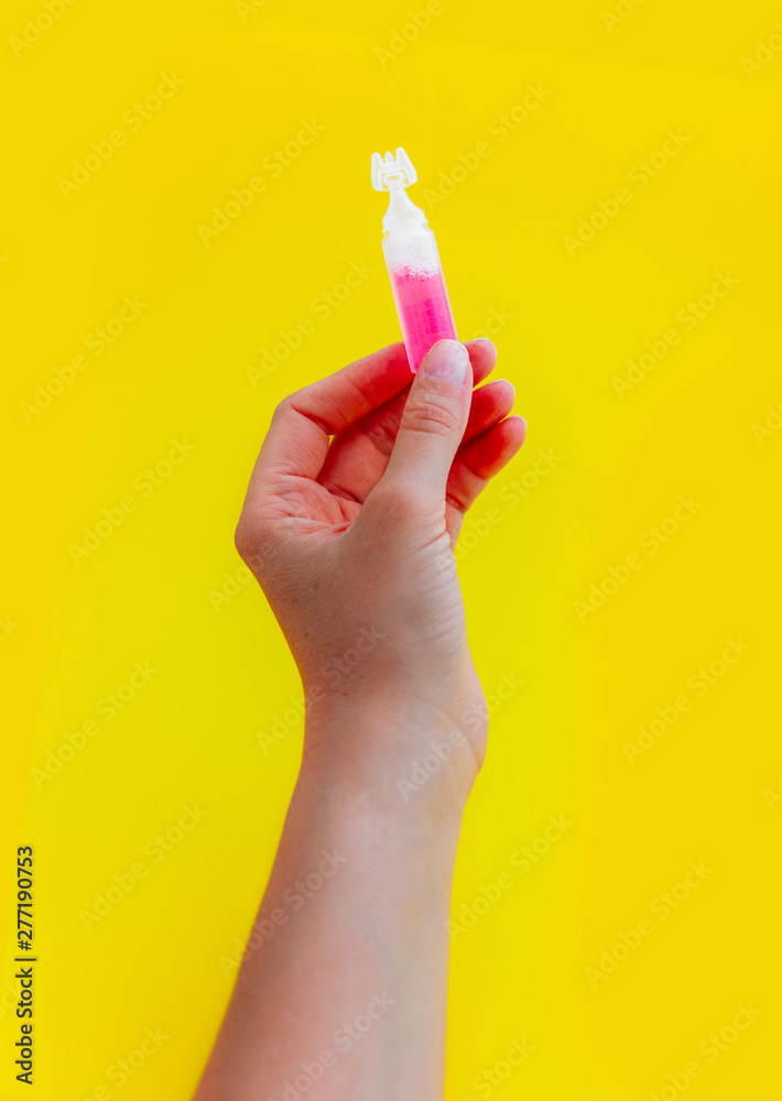 Female hand holding one pink liquid medicine in an ampoule, isolated on yellow background. Female hand holding one pink liquid medicine in an ampoule, isolated on yellow background.