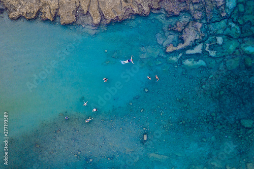 An aerial view of the beautiful Mediterranean sea  full of swimmers  where you can see the rocky textured underwater corals and the clean turquoise water of Protaras  Cyprus