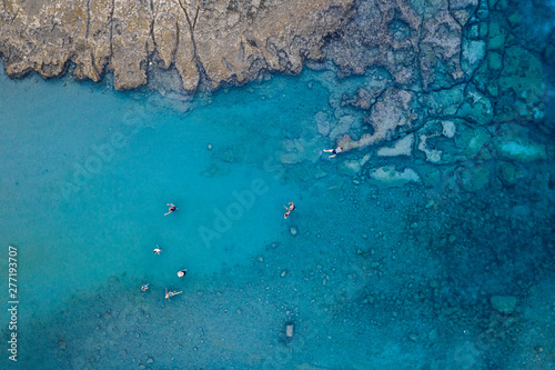 An aerial view of the beautiful Mediterranean sea, full of swimmers, where you can see the rocky textured underwater corals and the clean turquoise water of Protaras, Cyprus