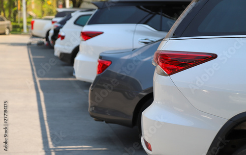 Closeup of rear, back side of white car with other cars parking in outdoor parking lot in bright sunny day. 