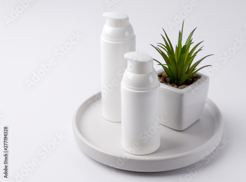 Cosmetic cream bottles with plant on the day at white table.