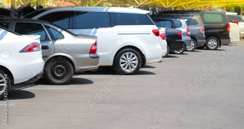 Closeup of rear, back side of white car with other cars parking in parking lo in bright sunny day. 