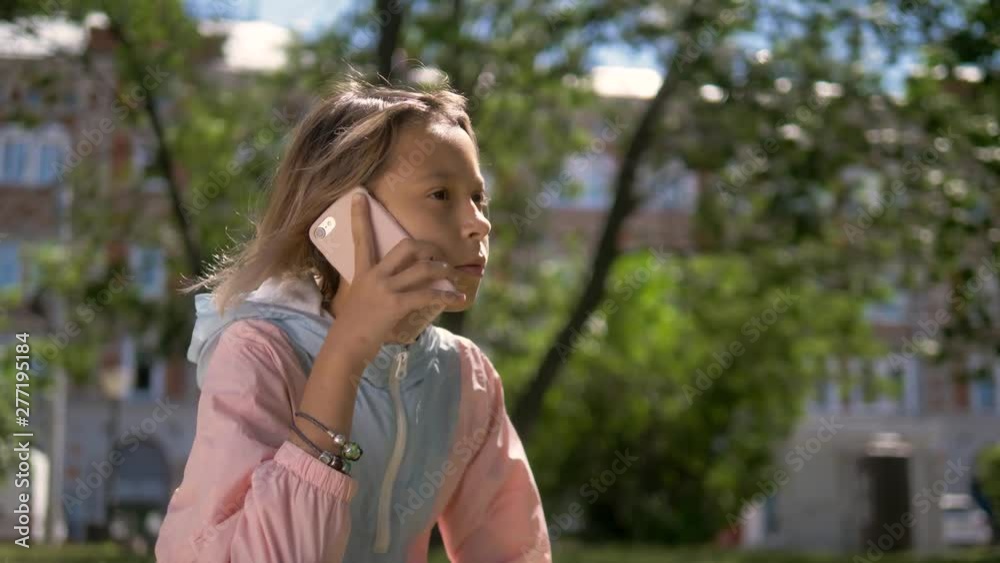 Beautiful little girl is talking on a phone and lying on a green. Grass on a sunny summer day Beautiful little girl is talking on a phone and lying on a green. Grass on a sunny summer day